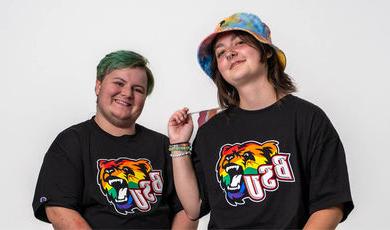Two students standing wearing black tshirts with rainbow bears on the front 